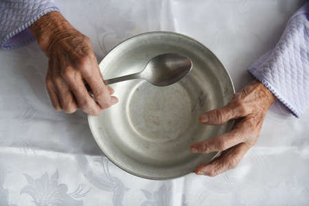 View from above.The hands of an old grandmother of 90 years are holding an empty aluminum bowl and spoon, poverty and poverty, the hunger of the older generation.の写真素材