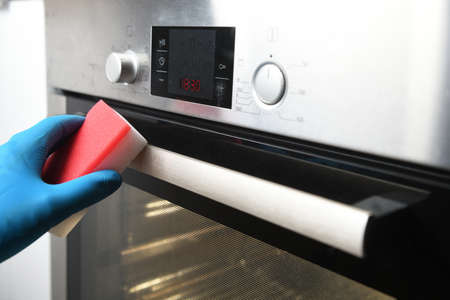 Cleaning the oven outside. Close up of female hands with protective gloves cleaning oven door. Girl...