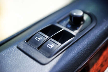 Detail on buttons controlling the windows in a car. Car interior details of door handle with windows controls and electric mirrors adjustments. Car tinted window controls and folding mirror detailsの写真素材