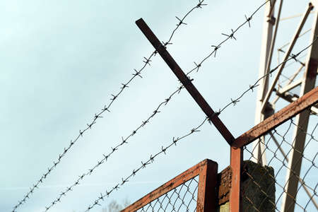 Barbed wire fence on blue sky background, closeup. Space for text