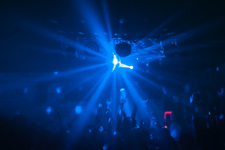 View of a party with bright disco ball sphere, people dance and raise handsの写真素材