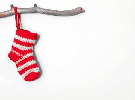 Christmas sock in a white-red strip hanging on a wooden branch on a white backgroundの写真素材