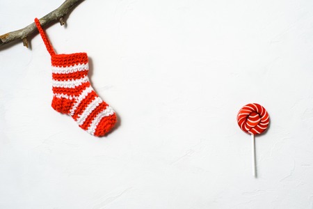 Christmas sock in a white-red strip hanging on a branch and red lollipop on a white background
