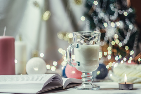 Romantic winter and New Year's style interior decoration with a candle, book, garland and glass of milkの写真素材