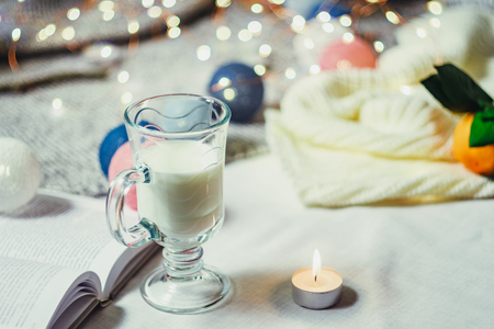 Romantic winter and New Year's style interior decoration with a candle, book, garland, cake and glass of milkの写真素材