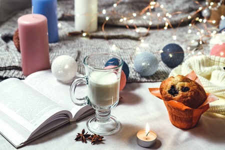 Romantic winter and New Year's style interior decoration with a candle, book, garland, cake and glass of milkの写真素材