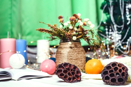 Romantic winter and New Year's style interior decoration with a candle, book, garland and dryed flowers in rustic vaseの写真素材