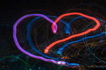 Bright glow abstract heart shaped patterns from light strips on a black backgroundの写真素材