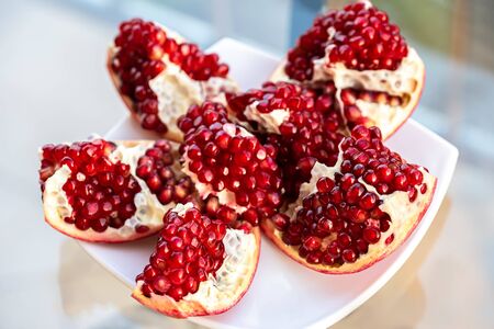 The fresh red tasty opened pomegranate on a white dish closeupの写真素材