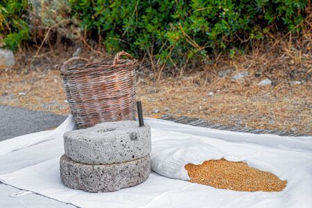 Rural surroundings - the Basket, wheat grains and a manual ancient stone mill on a white sheet