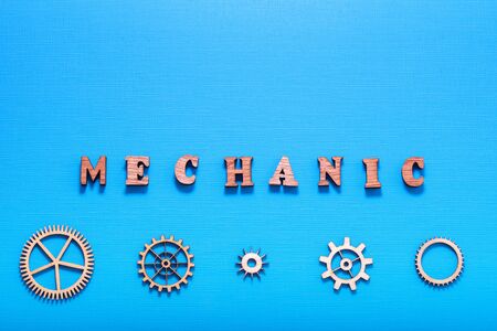 Word Mechanic written with wooden letters near wooden heavy machinery parts. Industrial style. Isolated on blue background.の写真素材