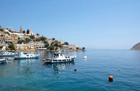 Symi, Greece - June 27, 2019: View of the coast of Symi island with town with multicolored houses, trees and peoples and bay with boats in summer dayのeditorial素材