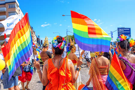 Stockholm, Sweden - August 2, 2019: People on the street prepairing to a Pride parade. Thai girls hold the rainbow flags, view from the backのeditorial素材