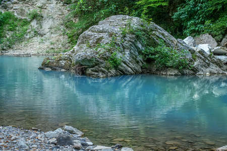 Motion blurred rapids of Khosta River with wet boulders and shore strewn with dry leaves and green trees arroundの写真素材