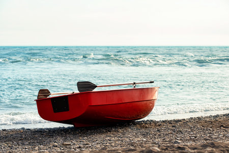 Small red rowboat with sculls lying at shore of the seaの写真素材