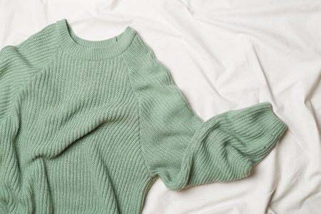 Warm green knitted sweater on white bed sheet. top view.