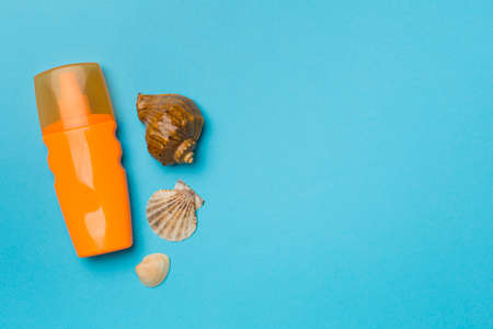 Bottle with sun protection cream and sea shells on color background, top view.