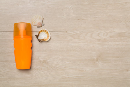 Bottle with sun protection cream and sea shells on wooden background, top view.の写真素材