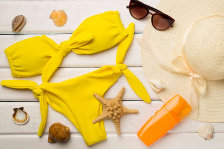 Beautiful yellow bikini and accessories on color wooden background, top view.