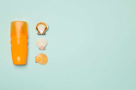 Bottle with sun protection cream and sea shells on color background, top view.