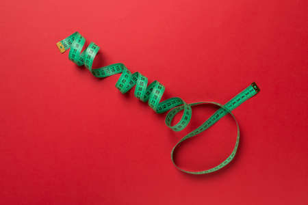 Green measuring tape on color background, top view.