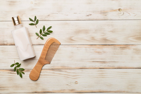 Shampoo with herbal extract and comb on wooden background, top view.