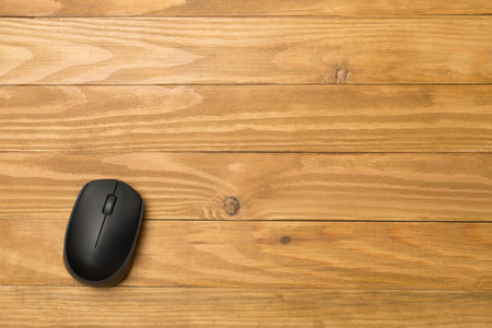 Black wireless mouse on wooden background, top view.