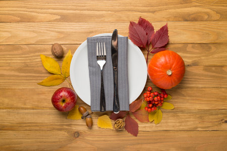 Plate with cutlery, napkin and autumn decor on wooden background, top view. Thanksgiving table setting.の写真素材