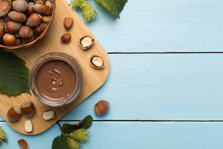Hazelnut cream with nuts and green leaves on wooden background, top view.