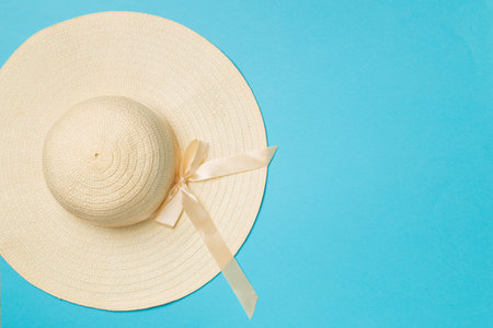 Beautiful straw hat with ribbon and bow on color background, top view.の写真素材