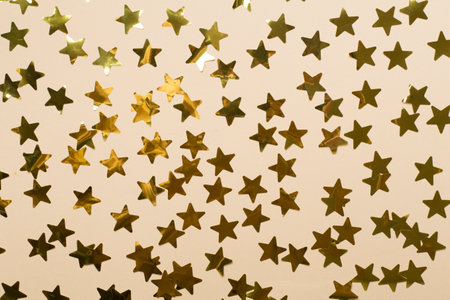 Golden confetti stars on color background, top view.