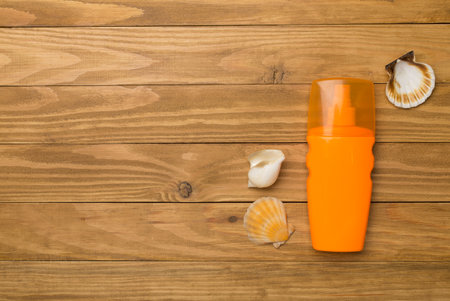 Bottle with sun protection cream and sea shells on wooden background, top view.の写真素材