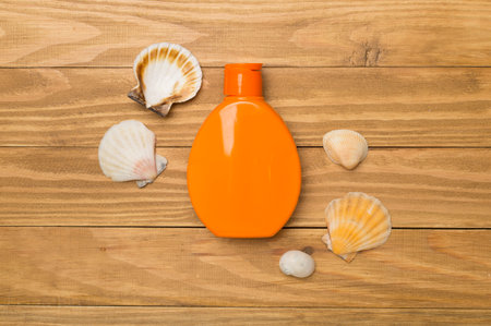 Bottle with sun protection cream and sea shells on wooden background, top view.