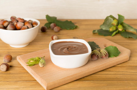 Hazelnut cream with nuts and green leaves on wooden table.の写真素材