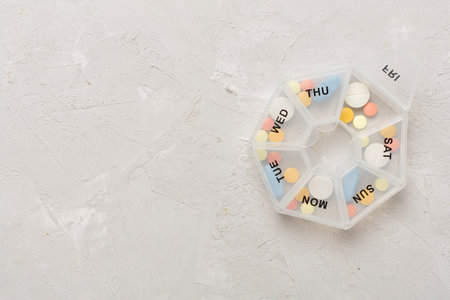 Daily pill organizer with medications on concrete background, top view