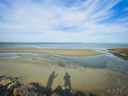 Couple taking photo on the beach at low tide with blue skyの写真素材