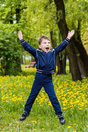 Smiling happy boy is jumping on green background on green fieldの写真素材