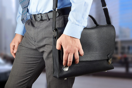 Businessman walking and holding  a  leather briefcase in his hand.  Modern city behindの写真素材