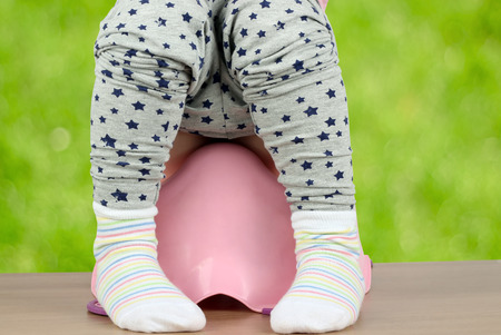 Children's legs hanging down from a chamber-pot on a green backgroundの写真素材
