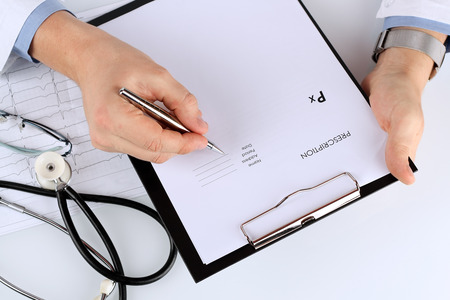 young medical doctor prescribing something/ Cardiogram of the heart and phonendoscope behindの写真素材