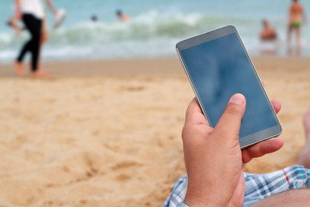 Man holding a mobile phone. internet connection on the beach. Sea behindの写真素材