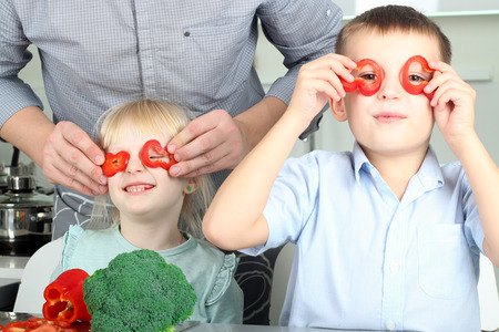 Smiling cute daughter and son  cooking  a  dinner. Little children  playing with colorful pepper with father.の写真素材