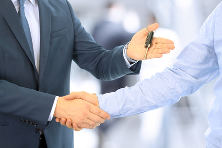 Car salesman handing over the keys for a new car to a young businessman . Handshake between two business people. Focus on a keyの写真素材