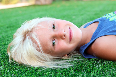 beautiful blonde smiling  girl  sitting  on the grass on a summer dayの写真素材