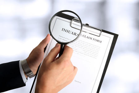 man looking through a  magnifying glass  to the Blank insurance claim formの写真素材