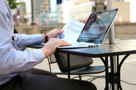 Business man working and analyzing financial figures on a graphs on a laptop outside