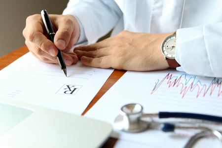doctor working on a computer at his cabinet / writing prescriptonの写真素材