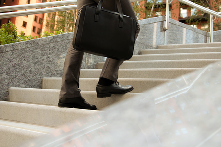 Businessman walking and holding  a  leather briefcase in his handの写真素材