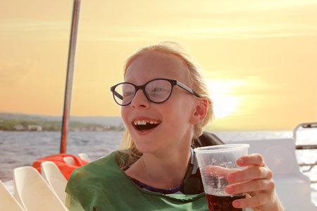 Young blonde girl in glasses have fun discovering islands on summer coastal cruise. Travel adventure, yachting with kids on family vacation.の写真素材