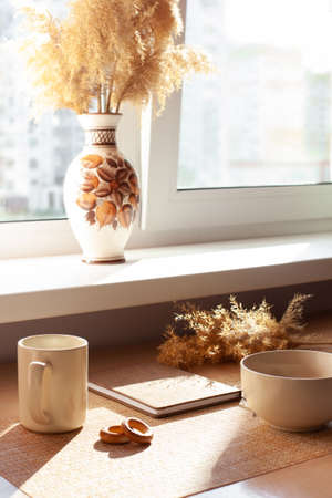 A cup of coffee, dry flowers, barankis, notepad on wooden table. Brown and white.